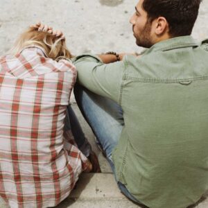 Man and woman sitting down next to each other on sidewalk