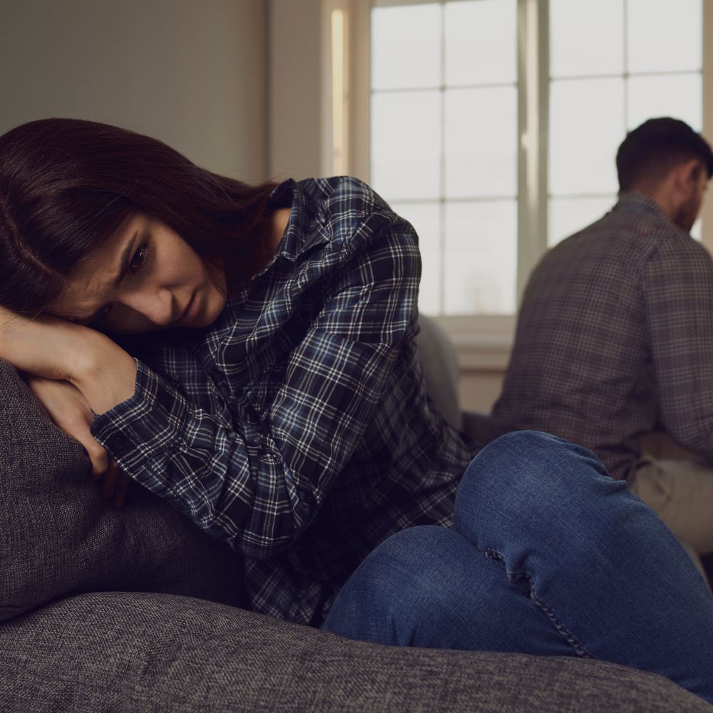 Sad woman on couch and man turned away behind her.