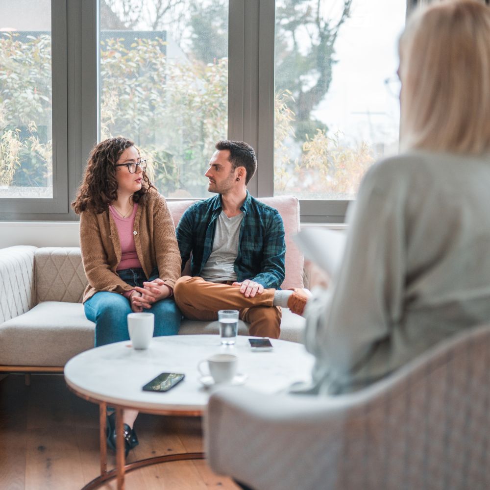 Couple sits close and sharing openly in warm therapy space