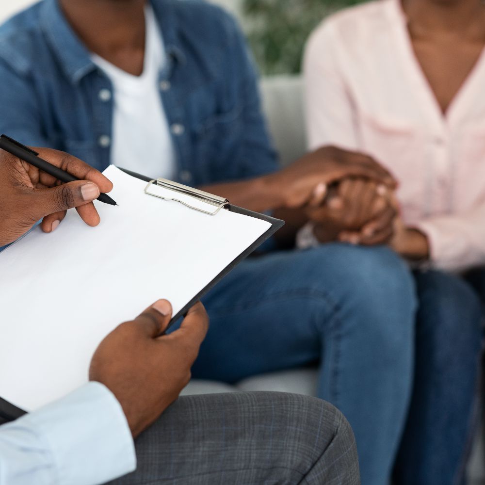 Therapist taking notes while couple holds hands during session