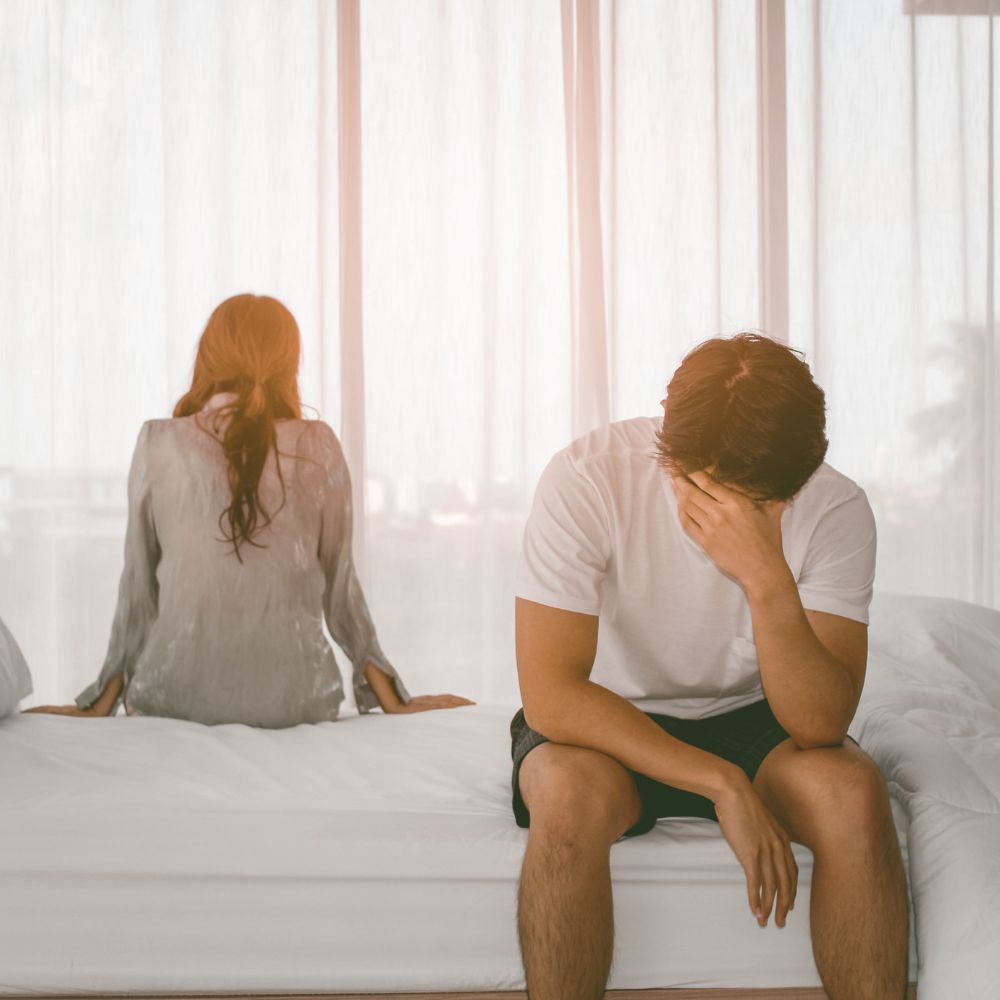 Sad couple facing away and sitting on bed silently