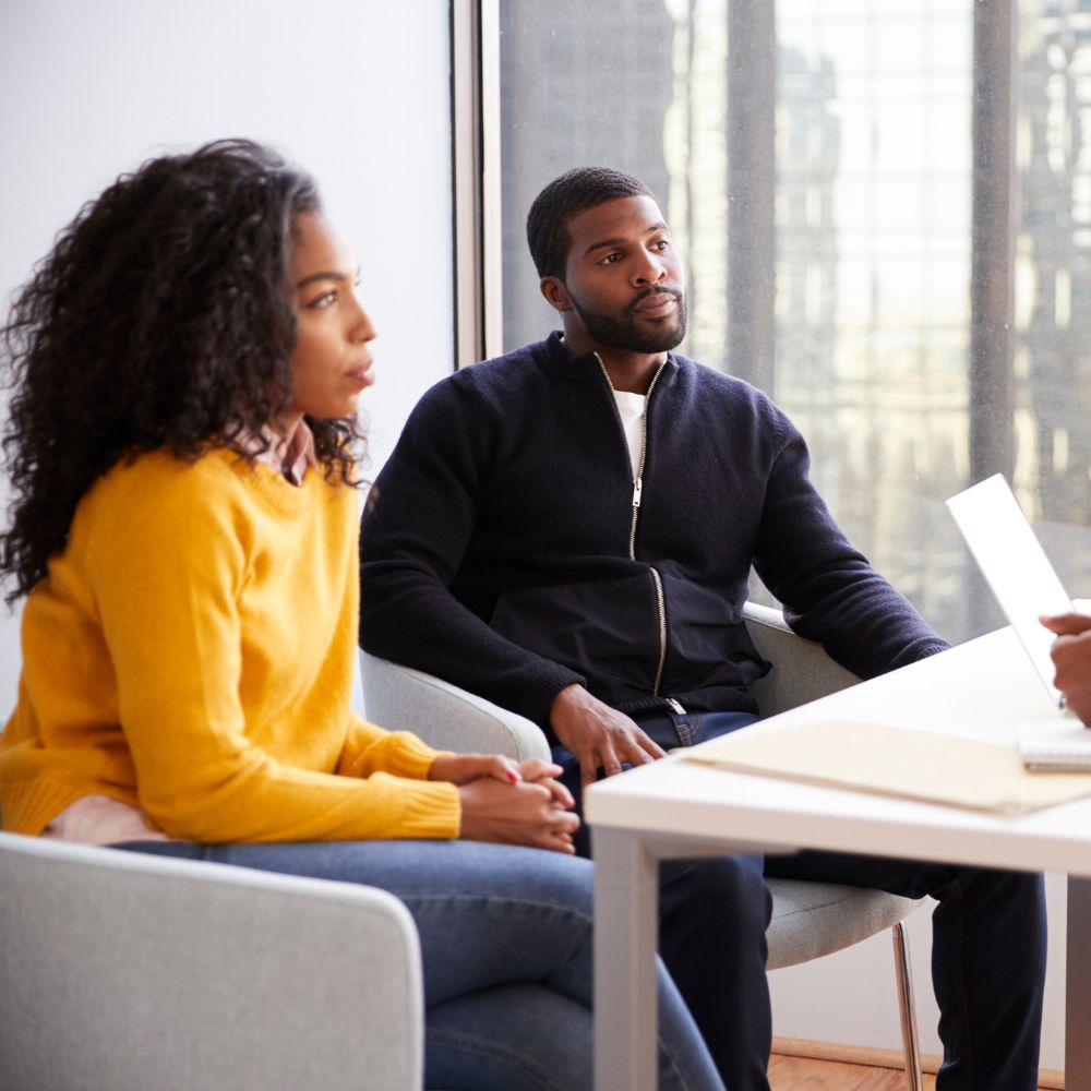 Couple sitting at office desk, engaged in serious conversation with counselor