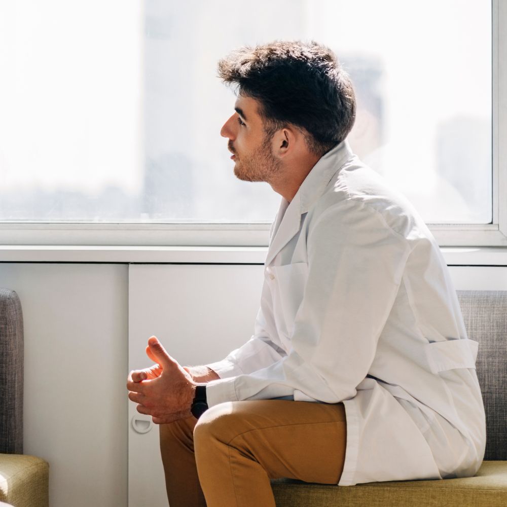 Male therapist in white coat listening attentively near bright window