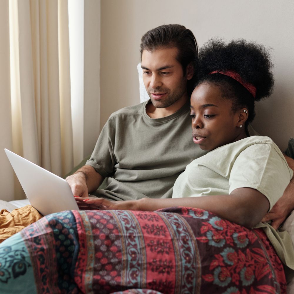 Couple relaxing together in bed using laptop computer