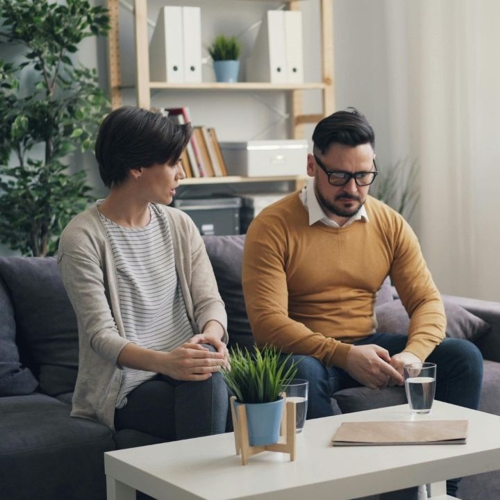 Couple sitting apart on a couch, looking serious and contemplative during a counseling session