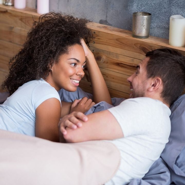 Couple smiling and looking at each other lovingly while lying in bed together