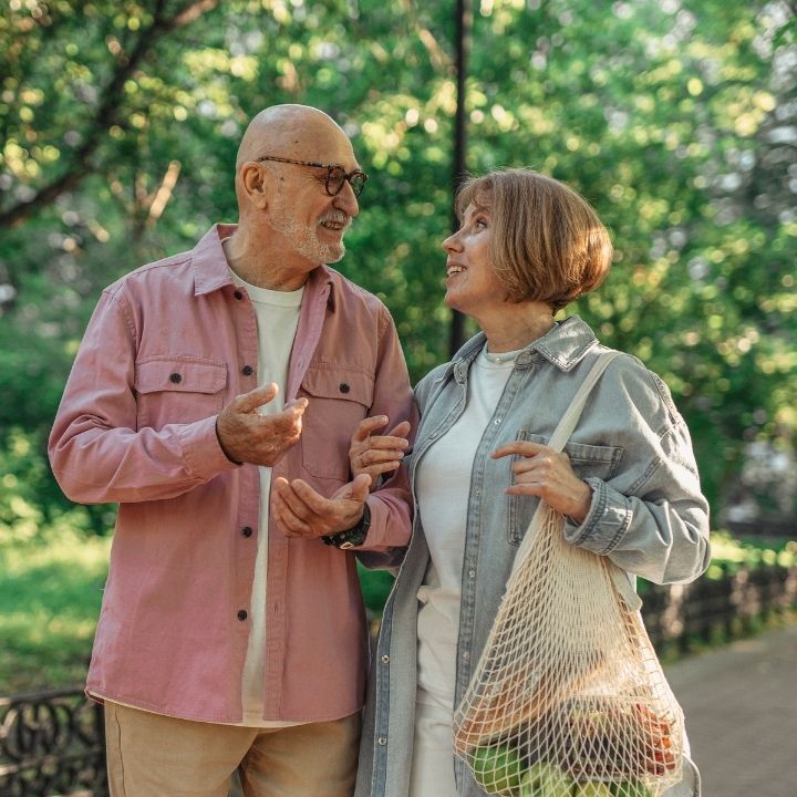 Elderly couple walking hand-in-hand in a park smiling