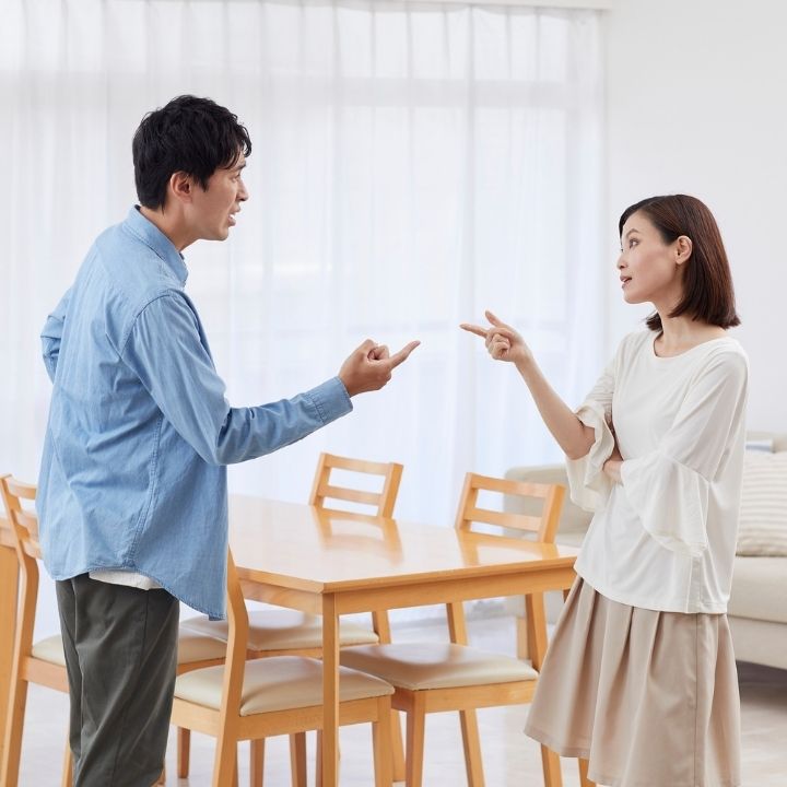 Couple arguing at home, both pointing at each other with visible tension between them