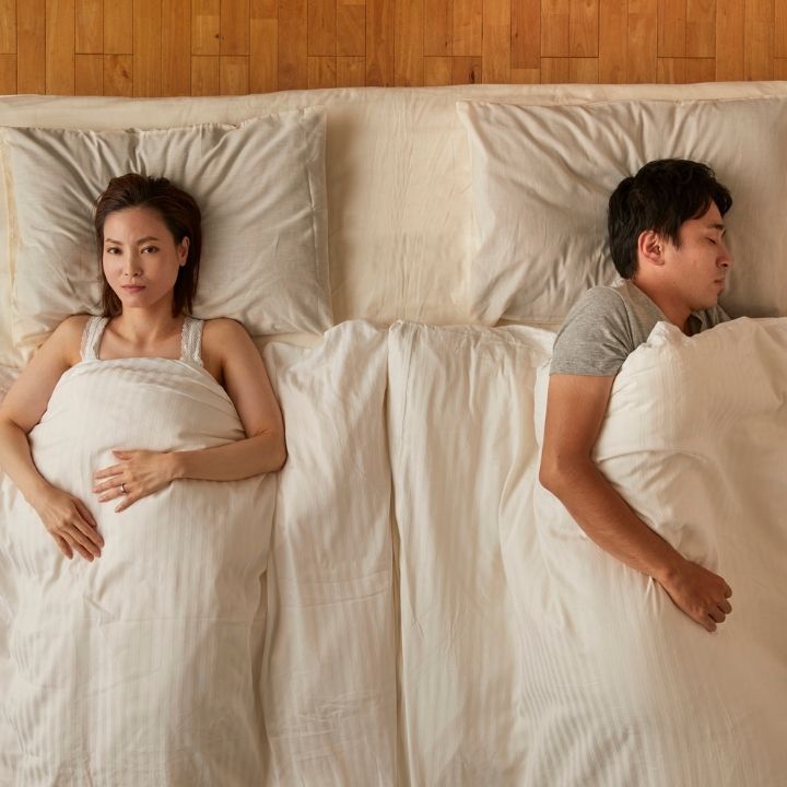 Couple lying in bed, facing away from each other