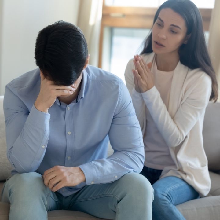 Woman pleading with her partner sitting with his head in his hands looking down in frustration
