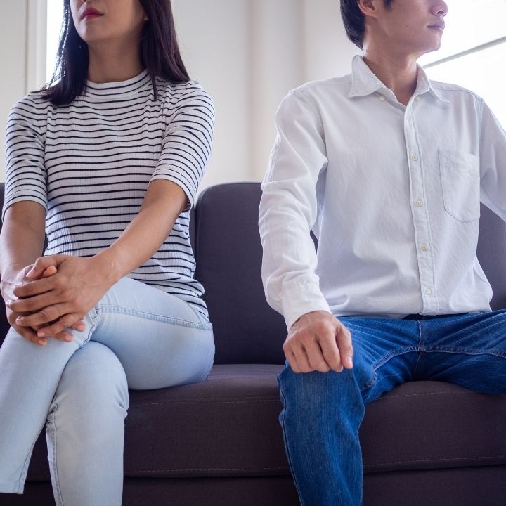 Couple sitting apart on a couch both facing forward with serious expressions
