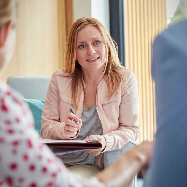 Female counselor attentively listening and taking notes during a session with a couple