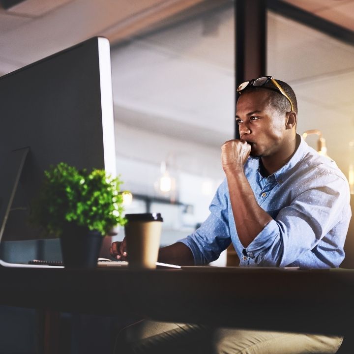 Male counselor in a dimly lit office looking thoughtfully at a computer screen