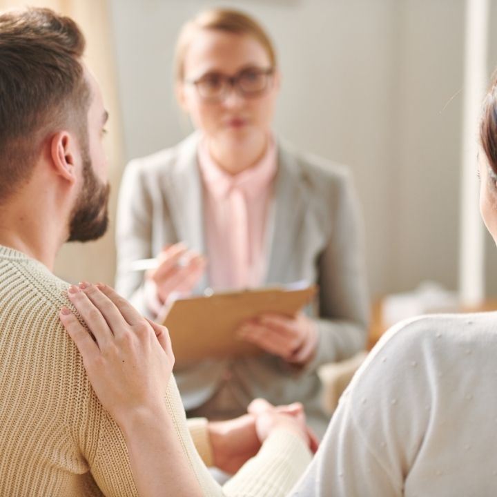 Couple holding hands during a counseling session with a professional taking notes