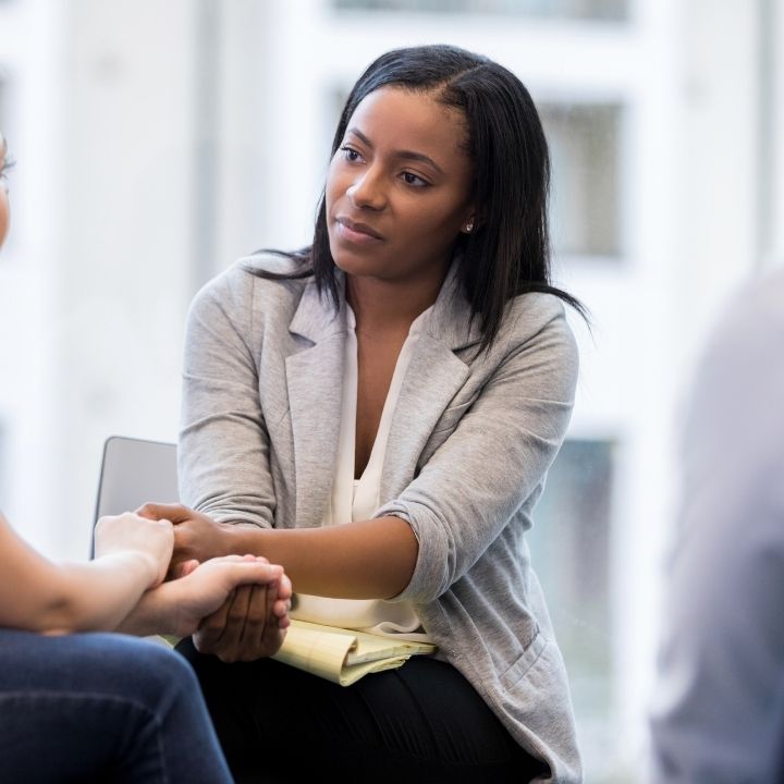 Counselor holding a client’s hands while offering support during a conversation