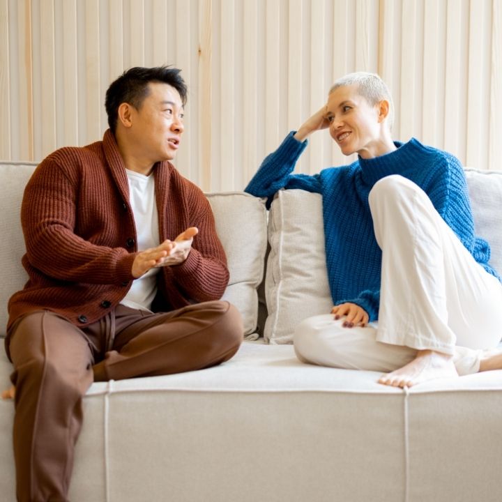 A couple sitting on a couch facing each other and talking in a relaxed home setting.